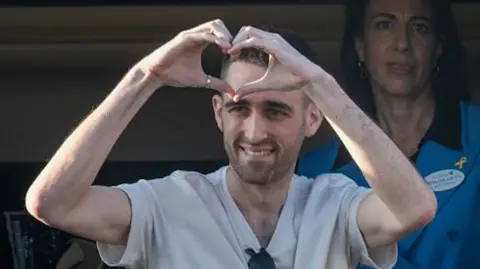 Getty Images A man in a grey T-shirt and sunglasses holds his hands in a heard position.