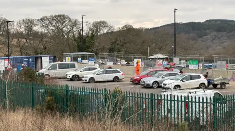 Lee Trewhela/LDRS Truro's household waste recycling centre. The sky is grey and cloudy in the background and there are workers in the background. There are cars parked in the bays used by people bringing their recycling to the centre. 