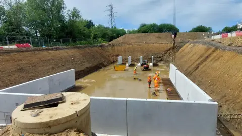 Leeds City Council The image shows a concrete water attenuation tank being installed. The surrounding walls are being put into place.