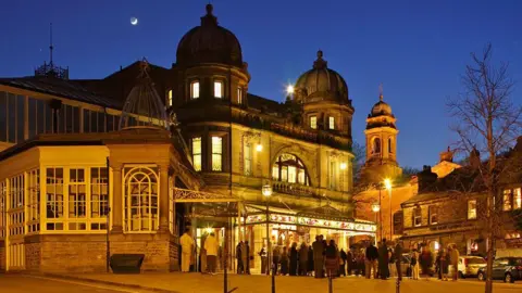 Buxton Opera House - a highly elaborate theatre building - lit up at night with queues outside the front entrance