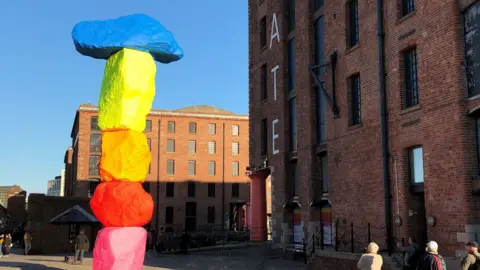 A large colourful scuplture outside of a brick building that has the word 'TATE' written on it.