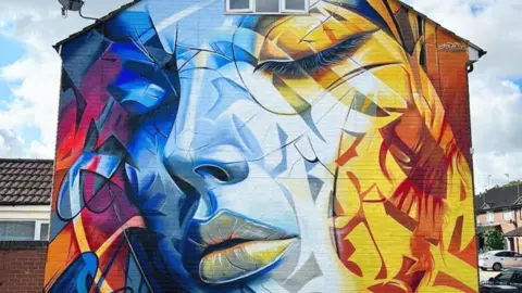 Ed Poster Colourful mural of a woman's face with closed eyes. Colours range from red and purple on the left to blue to yellow and orange on the right. The woman's face is blue, starting out more saturated on the left and becoming more fainted towards the right with her lips and left eye coloured yellow.