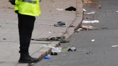 Jacob King/PA Wire Police officer standing at the scene near debris including shoes and blankets in Friar Gate, Derby, on Sunday 29 March 2026.