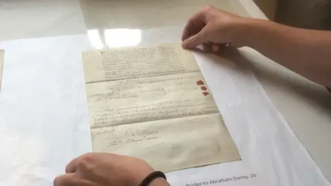 A pair of hands holding the corners of a piece of paper with some writing on it, on a white table top
