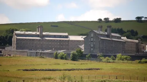 A view of Dartmoor Prison showing two large brick buildings surrounded by fields on a cloudy day.