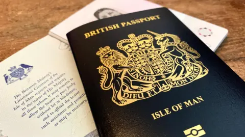 A black closed Isle of Man passport with gold writing, sitting on an open passport.