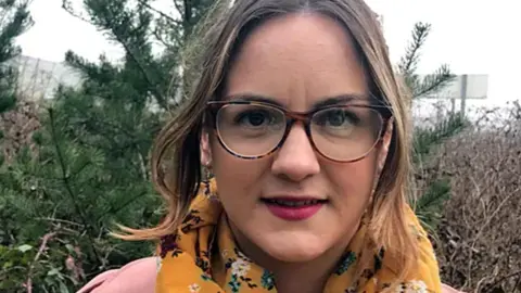 BBC Kirsty James wearing a pink coat and yellow floral scarf and glasses