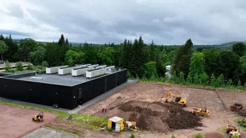 University of Edinburgh A building site of a new supercomputer. We can see a large black building, with several diggers next to it