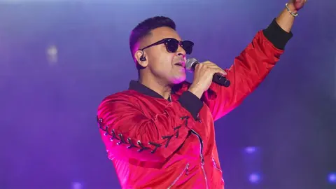 Getty Images Jay Sean, a man holding a microphone on stage, wearing a red fleece and sunglasses.
