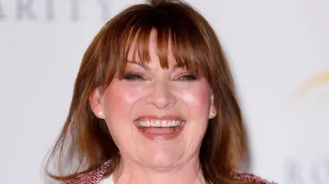 A close-up of a laughing Lorraine Kelly taken at an event. She wears glamorous makeup and a pink tweed jacket