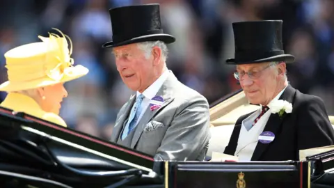 PA Media Queen Elizabeth II sits in an open carriage wearing a yellow hat. Lord Fellowes and the then-Prince Charles sit opposite her in suits and wearing black top hats