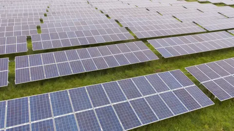 An aerial view of a row of solar panels in a field, surrounded by grass.