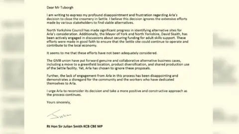'It's a dying town': Community hit hard by factory's loss 11 Supplied Screenshot of a letter from Julian Smith MP to Mr Peder Tuborgh, CEO of Arla. It reads: Dear Mr Tuborgh I am writing to express my profound disappointment and frustration regarding Arla’s decision to close the creamery in Settle. I believe this decision ignores the extensive efforts made by various stakeholders to find viable alternatives. North Yorkshire Council has made significant progress in identifying alternative sites for Arla’s consideration. Additionally, the Mayor of York and North Yorkshire, David Skaith, has been actively engaged in discussions about securing funding for adult skills support. These efforts were made in good faith to ensure that the Settle site could continue to operate and contribute to the local economy. It seems to me that these efforts have not been adequately considered. The GMB union have put forward genuine and collaborative alternative business cases, including a move to a greenfield location, product diversification, and shared production use of the Settle facility. Yet, Arla has chosen to ignore these proposals. Further, the lack of engagement from Arla in this process has been disappointing and demonstrates a disregard for the community and the workers who have dedicated themselves to Arla. I urge Arla to reconsider its decision and take a more positive and constructive approach as the process continues. Yours sincerely Rt Hon Sir Julian Smith KCB CBE MP