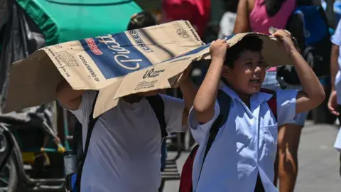 Getty Images Students in the Philippines' capital city Manila use a cardboard to protect themselves from the sun