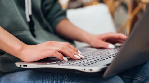 The image shows a woman's hands typing on a laptop.