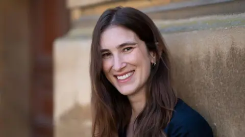 Katherine Rundell smiling, standing next to a stone wall