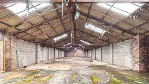 Shepherd A large empty warehouse with metal bars across the roof and panel windows