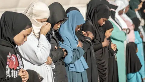 AFP Muslim women in headscarves stand in a row with their heads bowed in prayer near Johannesburg, South Africa