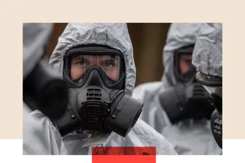 Getty Images Military personnel wearing protective suits with gas masks