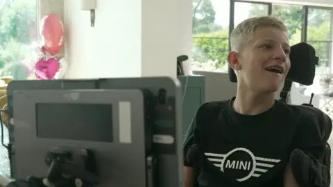 Boy with blond hair and black-shirt sitting in front of computer screen