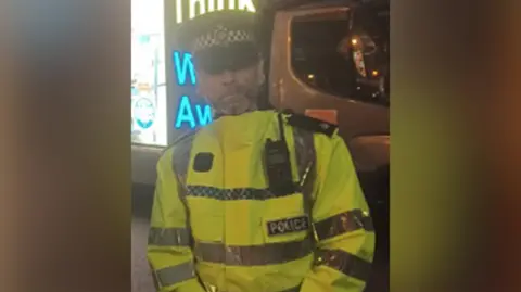 North Yorkshire Police A man wearing a police-branded high vis jacket and flat police cap with a short, greying beard