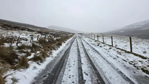 Shaele/BBC Weather Watchers White flush and snow covers road between fields on a grey day in Shetland.