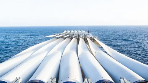 Getty Images A boat loaded with wind turbine blades on a blue sea.
