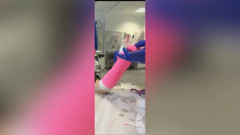 Family handout A close-up of someone's arm being wrapped in a pink bandage. The medic's hands are visible. A hospital room can be seen in the background. 