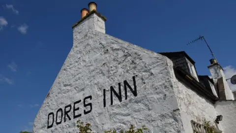 Getty Images A white-painted gable end of the Dores Inn. The words "Dores Inn" are painted in capitals on the wall.