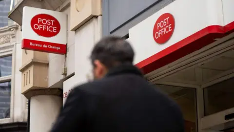 Getty Images Man in dark jacket walks past a Post Office branch