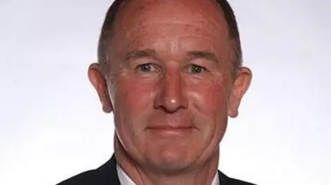 Councillor Tony Riordan. He is a middle-aged man with short brown hair and wearing a suit.