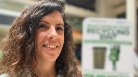 Emma Baugh/BBC A woman smiling at the camera. She has long, dark wavy hair.