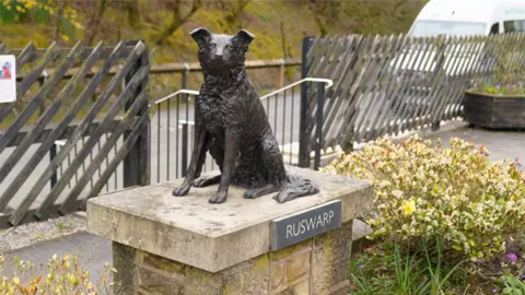 Nick Wooley/BBC A grey-bronze statue of a border collie sat on a stone plinth