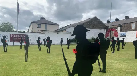 BBC/Phil Cunliffe Silhouettes of soldiers stand on Read Cricket Club - they are metal statues wearing poppies