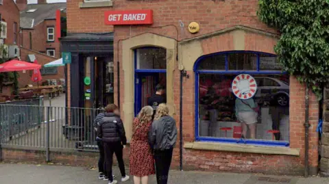 Google Customers stand outside a red brick building with a sign above the door reading Get Baked.