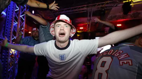 PA Media An England fan, in a red bucket hat, roars on the team with his arms outstretched