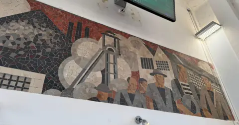A mural at train station of miners leaving a pit. It shows the male miners talking to each other and there is a large slag heap in the background.
