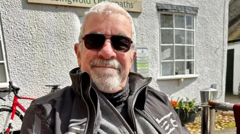 Handout A photo of Stephen Jackson, who is wearing motorcycling overalls and black aviator sunglasses. Jackson, who has short grey hair and a grey goatee, is smiling in the photo.