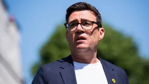PA Media And Burnham is starring off camera in this candid photograph. He is wearing a white T-shirt and dark grey jacket and has a yellow bee pin badge. 