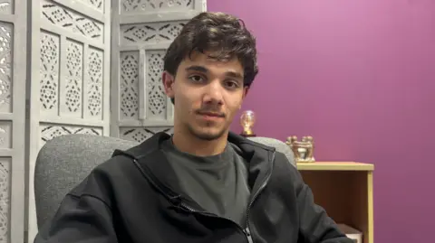 MOLLY SMITH / BBC NEWS Sammi has jet black hair and is wearing a dark grey t-shirt with a black zip up jacket. 