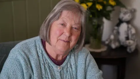 John Fairhall/BBC Joan James wearing a blue cardigan while looking into the camera. Her head is slightly tilted