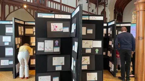 Two people look at a children's design display in a school hall