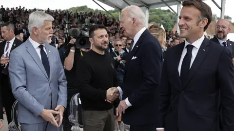 EPA-EFE/REX/Shutterstock Ukrainian President Volodymyr Zelensky and US President Joe Biden shake hands at a D-Day commemoration in Normandy