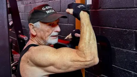 Mick Wadge flexes his right arm while using a weight-training machine at the gym.