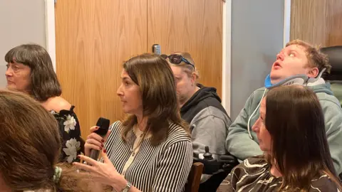 A woman with a striped top holding a microphone in an audience. 