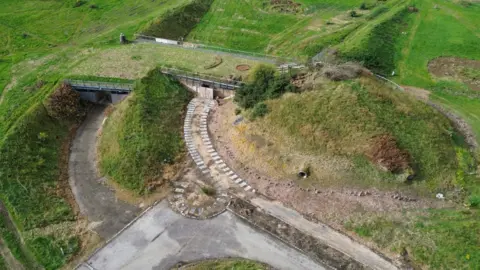 An aerial view of Archaeolink Prehistory Park. The building has a grass roof and blends into the rural landscape. 