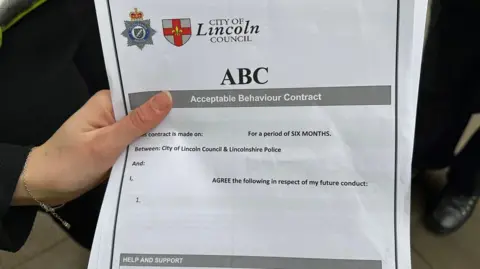 Leanne Brown/BBC A person holding an ABC form, which includes headings for details about what a young person will agree to in respect of their behaviour. It has the emblems of Lincolnshire Police and the city council at the top of the document.