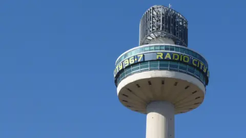 St Johns Beacon against a blue sky with Radio City 96.7 written in yellow.
