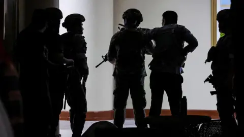 Reuters Silhouette of six soldiers standing and holding long firearms, their backs to the camera, in the Philippine Senate hallway.