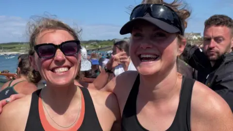 Two women in black singlets with their arms round each other laughing.